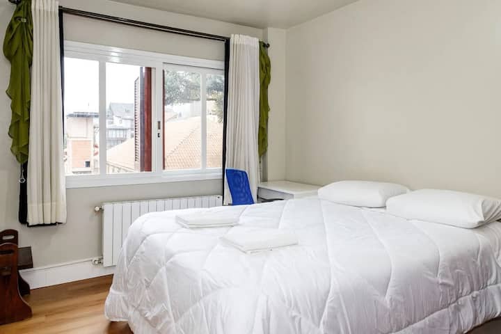 Quarto com cama queen, escrivaninha com cadeira, roupeiro, cortina black-out.