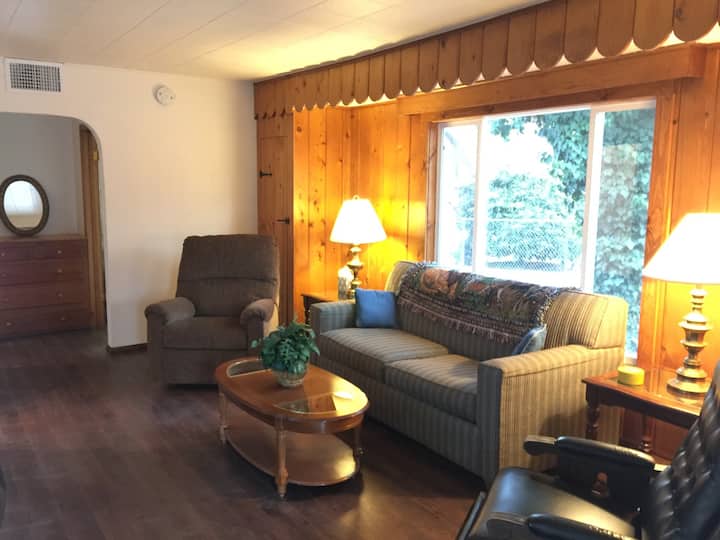 Our cozy family friendly living room, with vintage wood paneling wall detail. Sofa and chairs face our large screen TV.