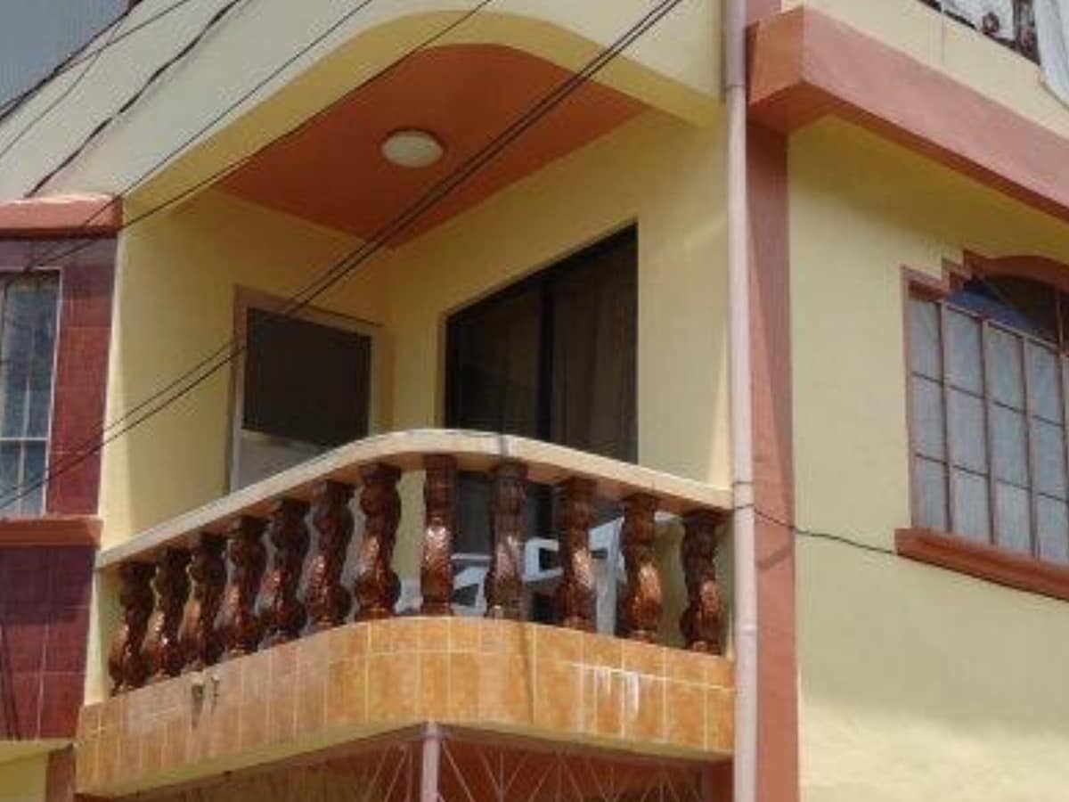 A charming exterior of the house features a spacious balcony with decorative railings, complemented by large windows that allow natural light. The warm color palette enhances the welcoming appearance. Air conditioning units can be seen on the left side, indicating a comfortable indoor environment.