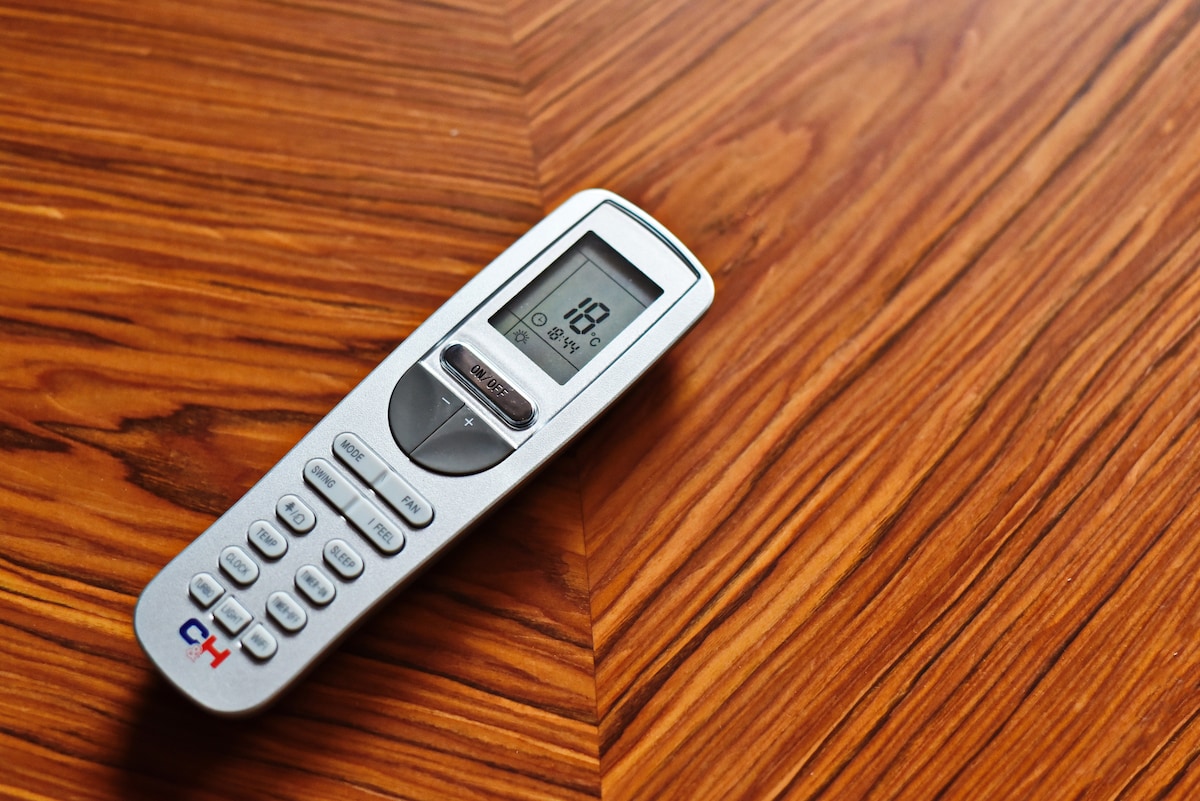 A remote control is positioned on a polished wooden surface, showcasing a rich grain pattern. The device has a digital display that indicates a temperature setting, with buttons arranged for easy operation.
