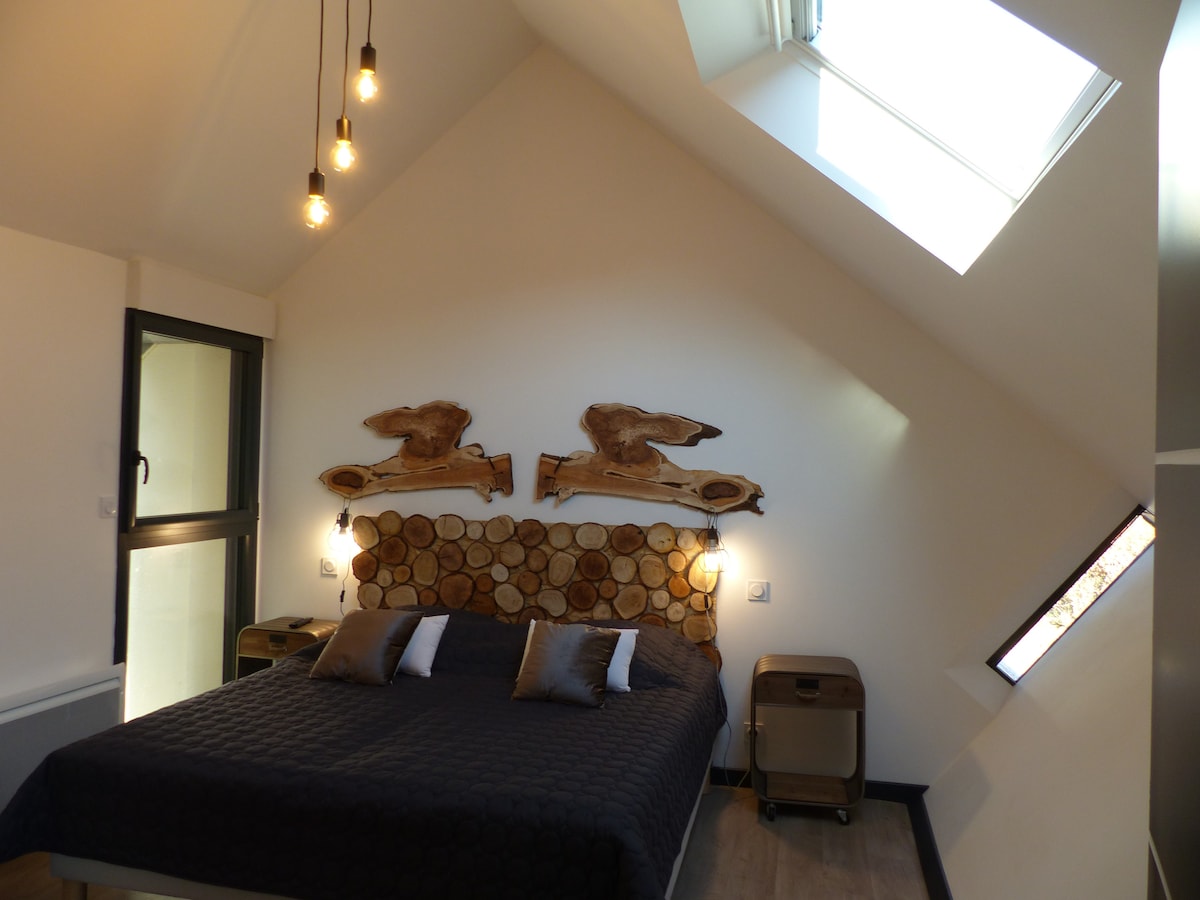 The bedroom features a spacious bed with a headboard crafted from natural wood slices. Large windows allow natural light to fill the room, while minimalist bedside tables complement the modern design. Unique pendant lights hang from the ceiling, enhancing the room's contemporary ambiance.