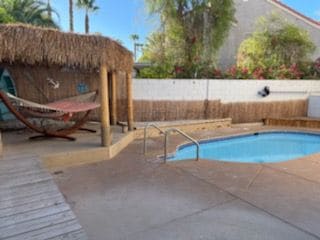 A private pool area is surrounded by a bamboo fence, featuring a small pool with steps leading in. A thatched-roof structure offers shade, accompanied by a hammock for relaxation. Lush greenery and flowering plants are visible in the background.