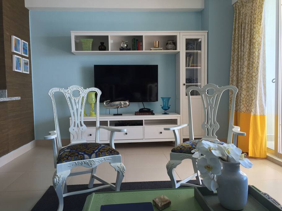 Large, cable TV sided by antique chairs and original abstract paintings