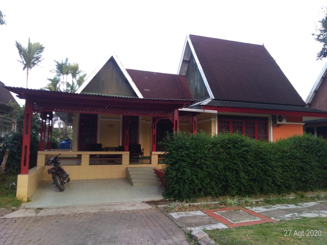 A charming house features a unique architectural style with a sloped roof and a welcoming porch area. The front yard is landscaped with low hedges and features a pathway of stone tiles. A motorcycle is parked near the entrance.