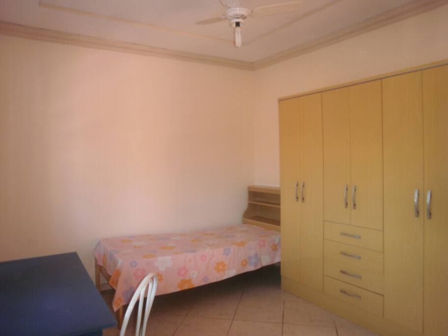 quarto com cama bau, escrivaninha, guarda roupa e ventilador de teto