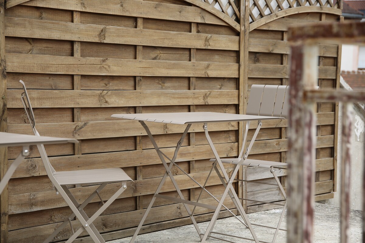 A garden terrace is seen featuring a small folding table accompanied by two matching folding chairs. The wooden fence in the background showcases a natural finish, enhancing the outdoor setting. The surface appears suitable for dining or relaxation.