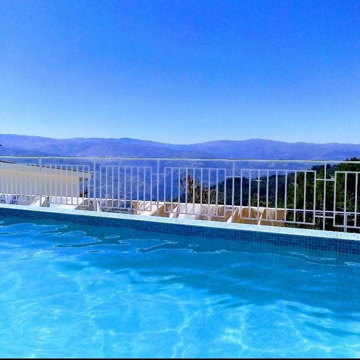 A private swimming pool is seen, set against a backdrop of expansive hills and a clear blue sky. The water is calm, reflecting the surrounding landscape. A white safety railing borders the pool area, enhancing safety while offering unobstructed views.