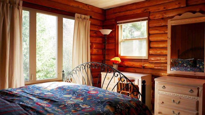 Chambre principale avec lit queen-size, petit bureau et chaise, coffre avec miroir de meuble vasque et placard.