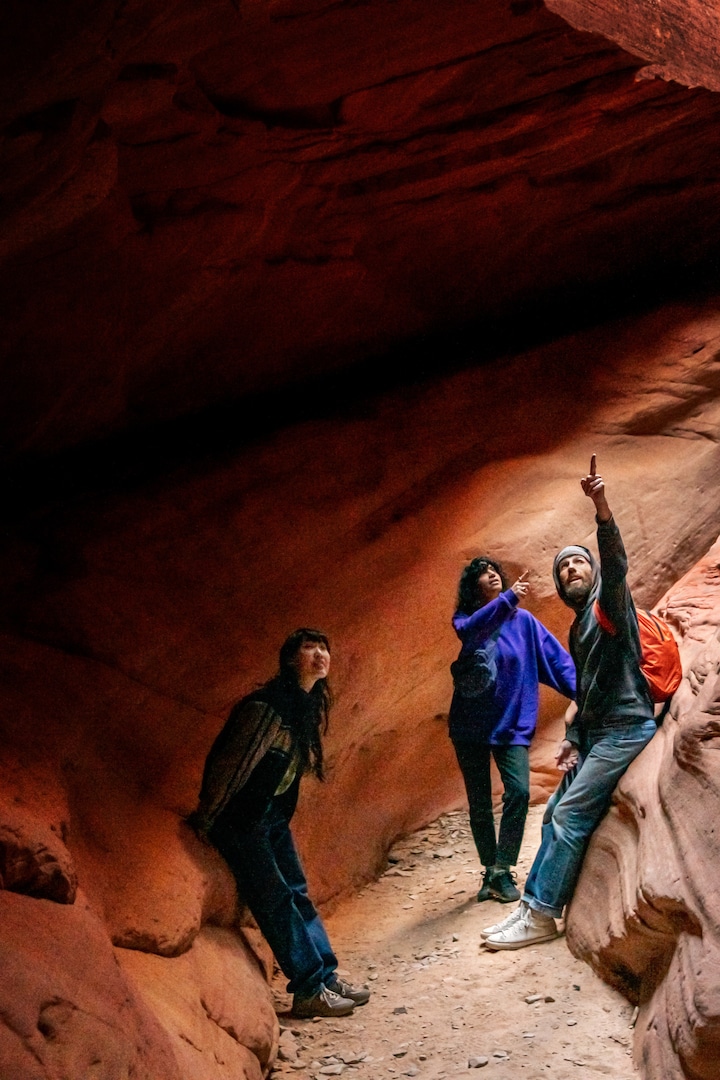 Trois personnes se trouvent dans un canyon de grès à Kanab, en Utah, aux États-Unis. L'hôte de l'expérience montre quelque chose en hauteur aux deux voyageurs.