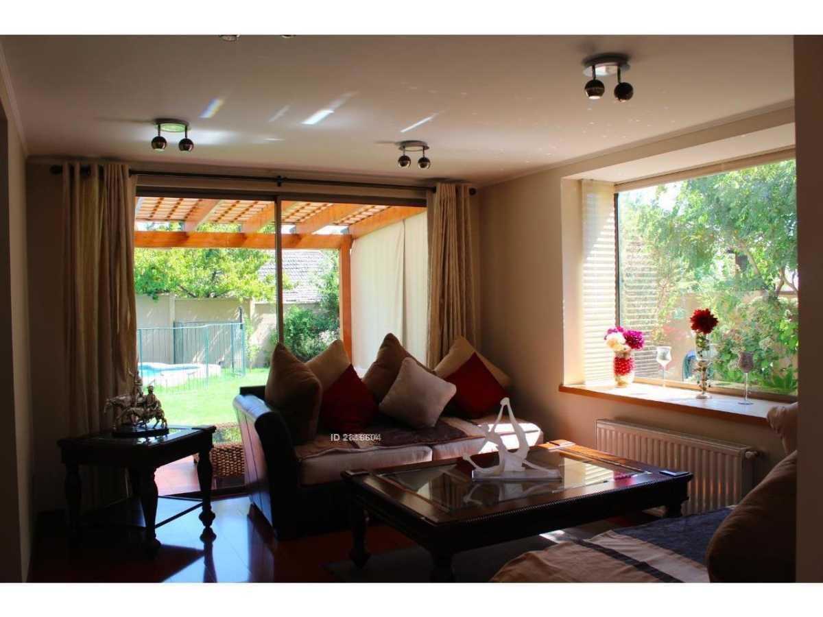A bright living area is depicted, featuring a comfortable sofa adorned with cushions and a medium-sized coffee table. Natural light streams through large windows, illuminating the space. Outside, a glimpse of greenery and a swimming pool can be seen through the glass doors.