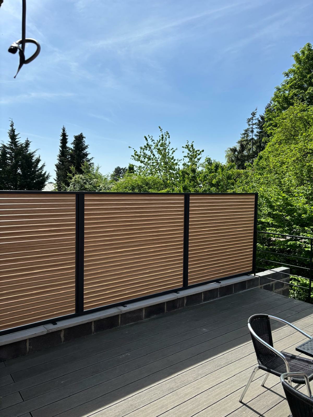 A private outdoor terrace is shown, featuring wooden fencing that offers privacy while complementing the surrounding greenery. The space includes a wooden deck and a seating arrangement, inviting relaxation amidst a tranquil natural setting.