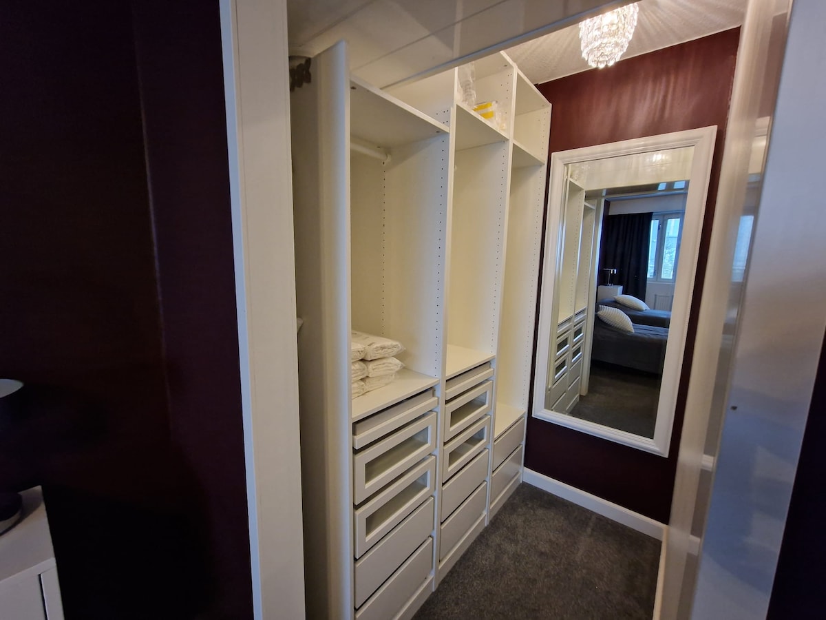 A well-organized closet features multiple shelves and drawers, providing ample storage space. Neatly stacked towels and various personal items are visible inside. A large mirror reflects the light from the room, enhancing the functionality of the space.