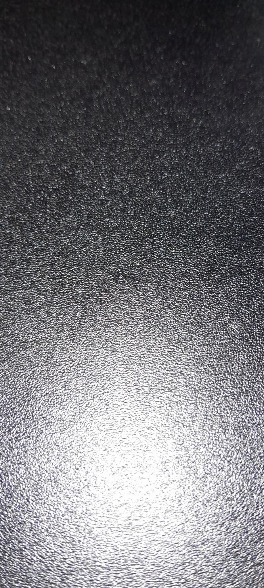 A close-up image shows a textured black surface. The surface exhibits a subtle sheen and fine detailing, creating a consistent visual effect that emphasizes its smoothness.
