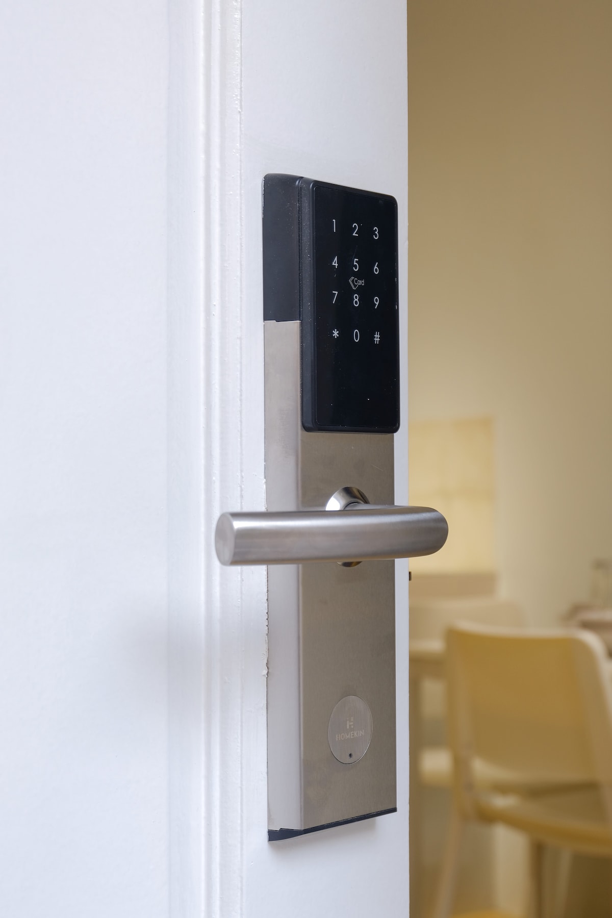 A close-up view of a modern electronic door lock is displayed, featuring a keypad with numerical buttons and a metallic lever handle. The lock is mounted on a white door, leading to an inviting interior, subtly indicated by soft light in the background.