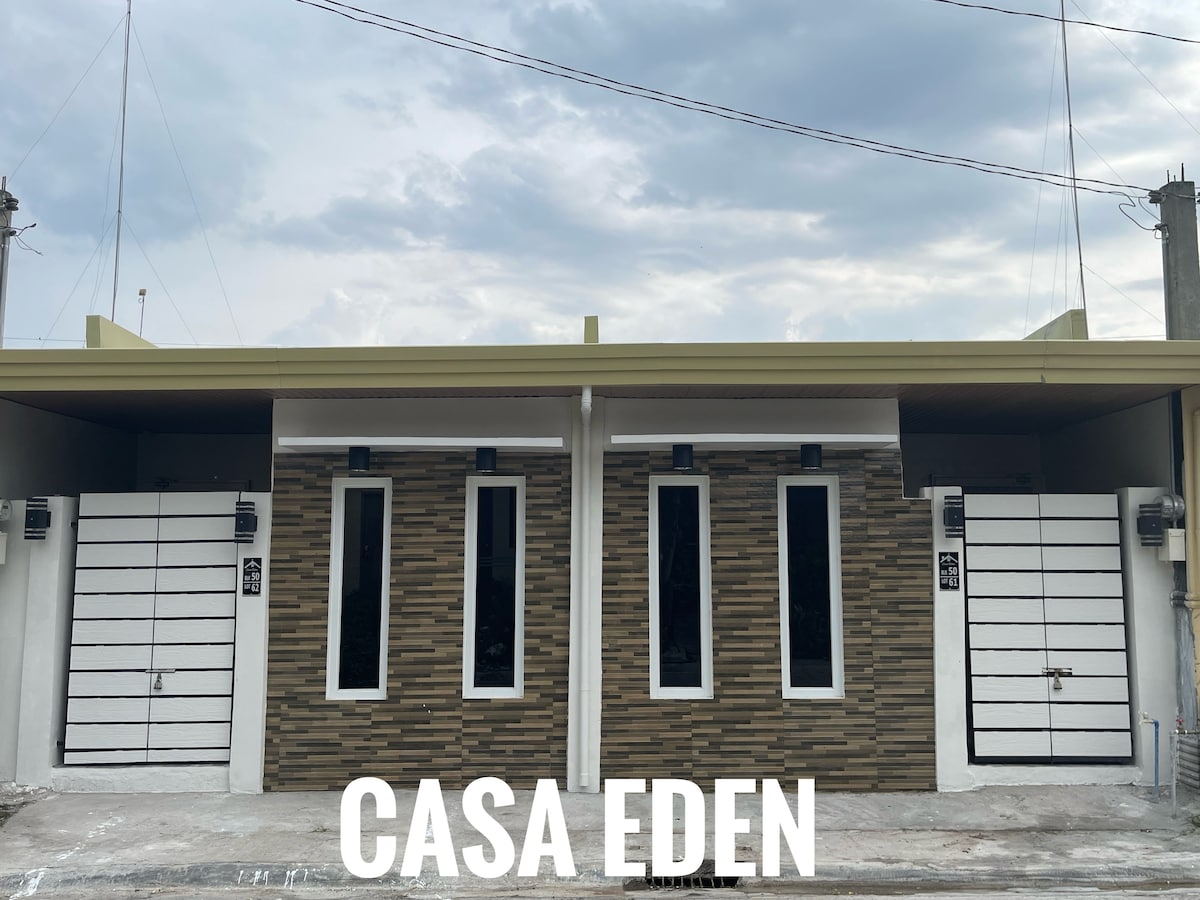 A modern exterior of the building is showcased, featuring two identical units with textured stone accents and sleek white doors. Tall, narrow windows framed in dark finishes allow natural light to enter. A clear sky with scattered clouds provides a contrasting backdrop.