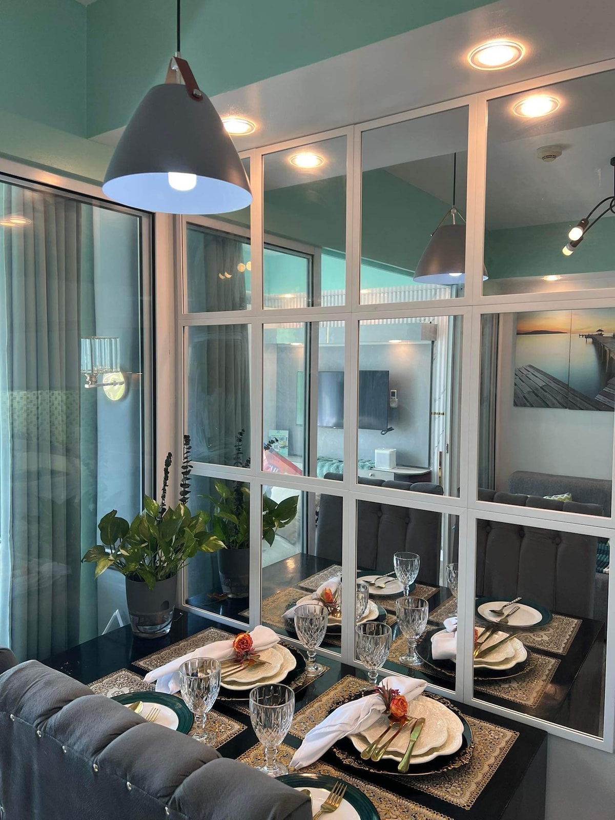 A dining area is highlighted by a mirrored wall and soft lighting. A table is elegantly set with plates, glassware, and cutlery, complemented by a small floral arrangement. The room's vibrant colors and modern decor create a fresh and inviting ambiance.