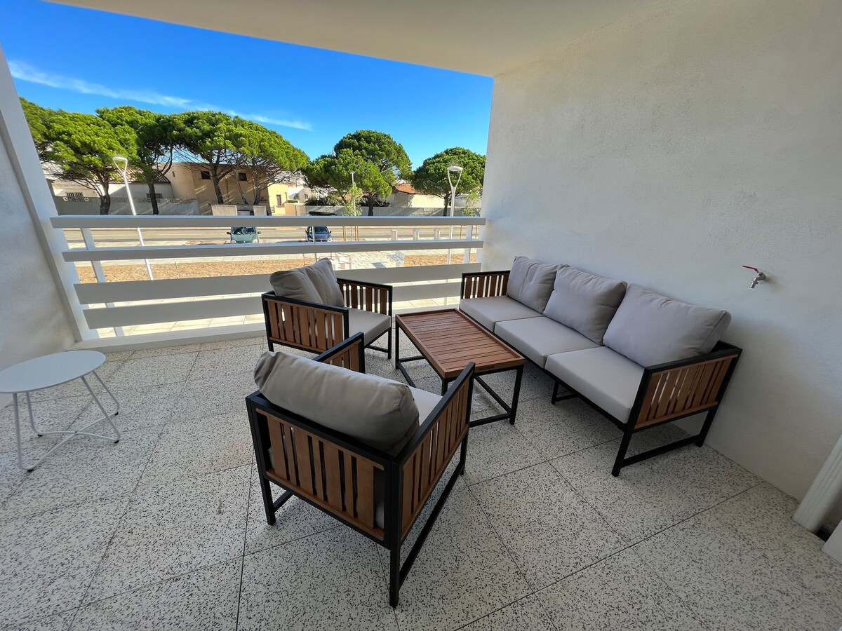A comfortable seating area features a sectional sofa and two armchairs with soft cushions. A wooden coffee table complements the arrangement. The space is situated outdoors, showcasing views of surrounding trees and a clear blue sky.