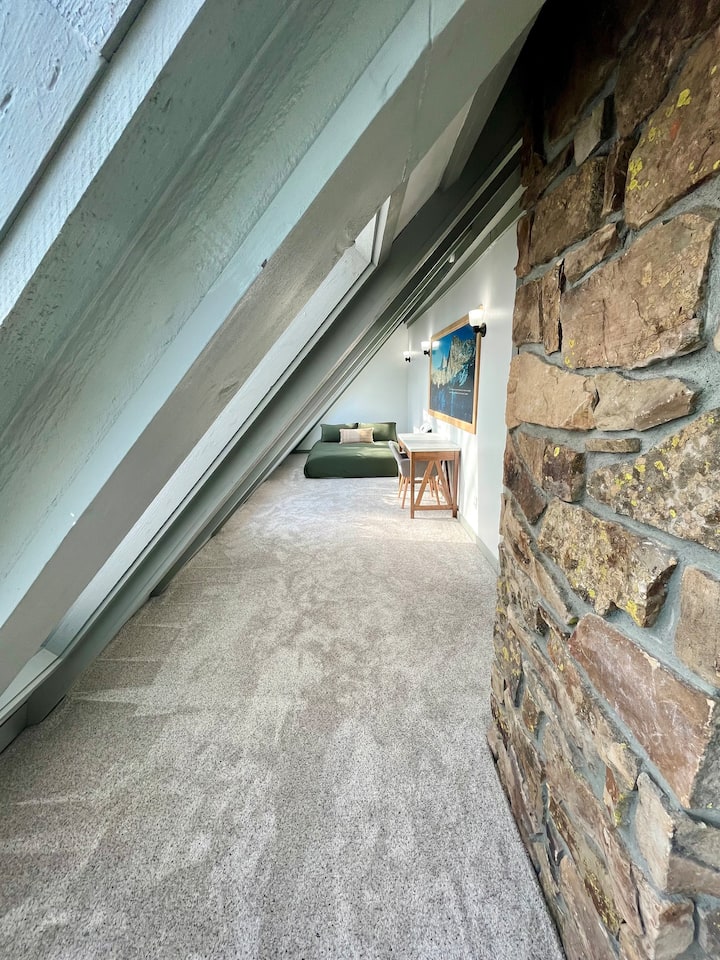 Slnečná miestnosť na poschodí s manželskou posteľou Queen a písacím stolom.