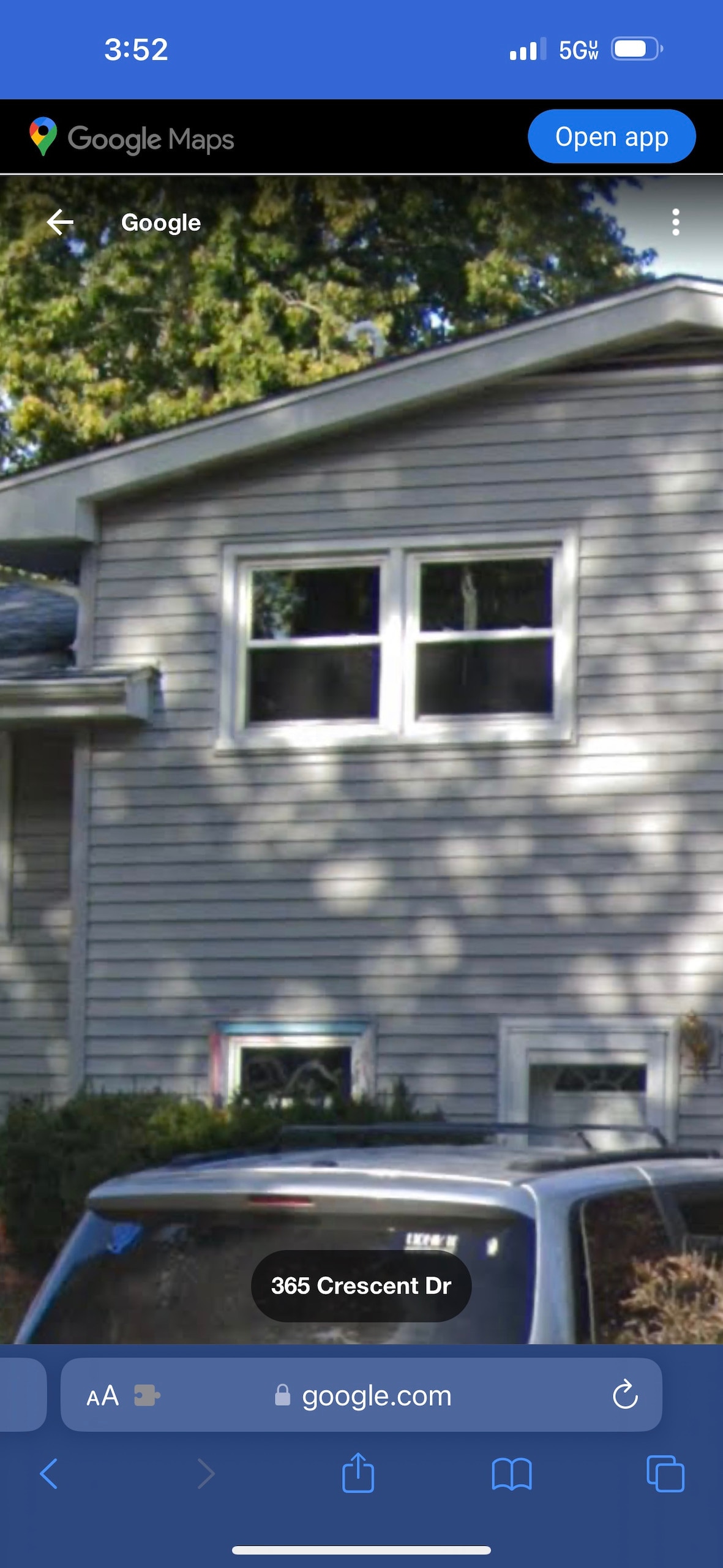A two-story house is depicted with a light gray exterior. Two symmetrical windows on the upper level allow natural light to fill the space, while a sloped roof adds to the structure's profile. The surrounding area features greenery and a parked vehicle in front.