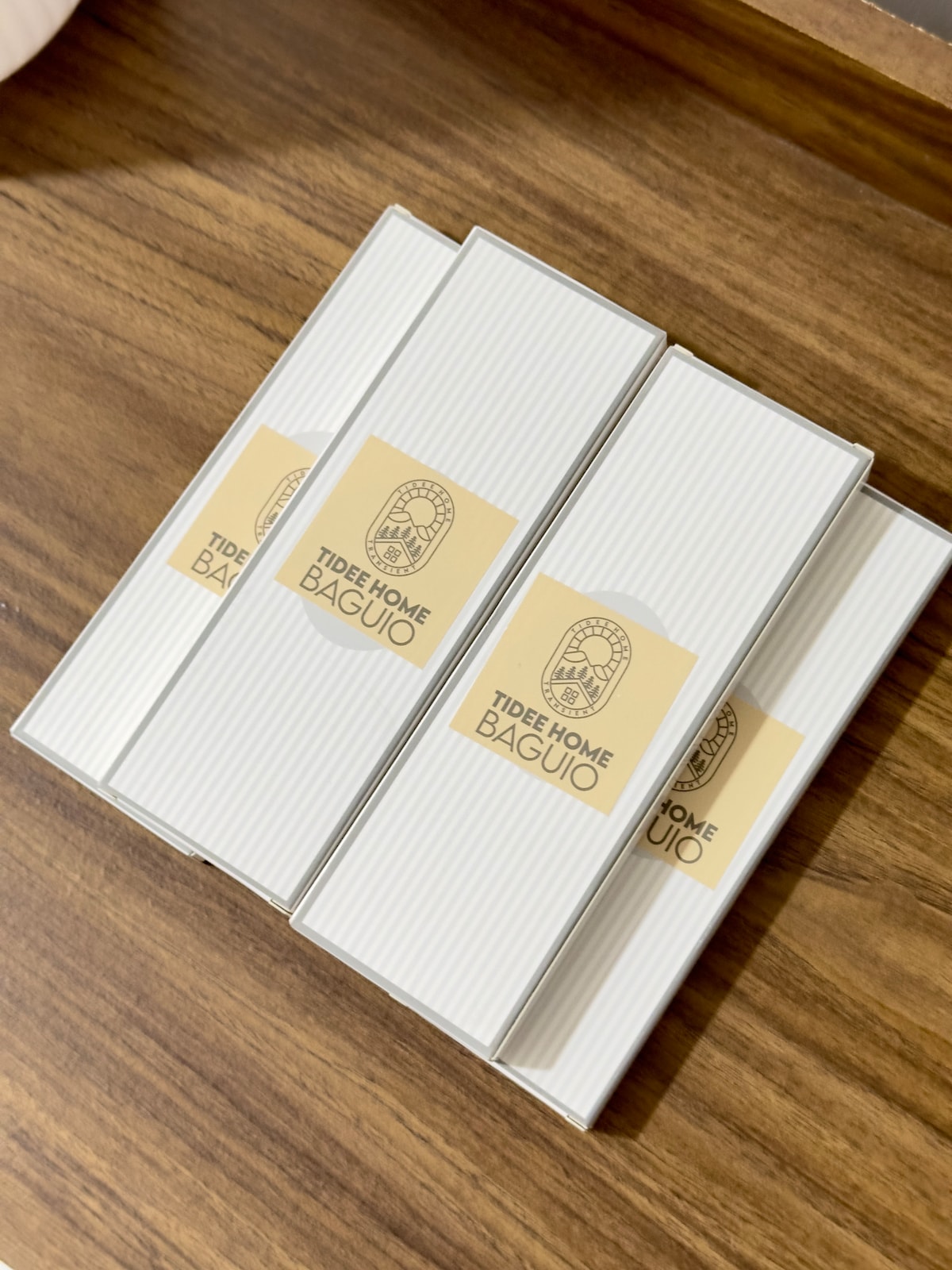 Four neatly arranged white boxes with striped texture are displayed on a wooden surface. Each box features a logo that reads 'Tide Home Baguio,' contributing to a clean and organized environment.