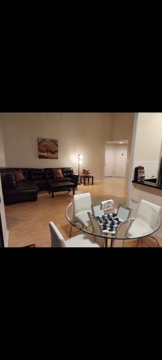 A cozy living area is visible, featuring a black leather sofa and a small table with white chairs. A soft glow emanates from a nearby lamp, highlighting a decorative piece on the wall. An open layout provides a sense of spaciousness.