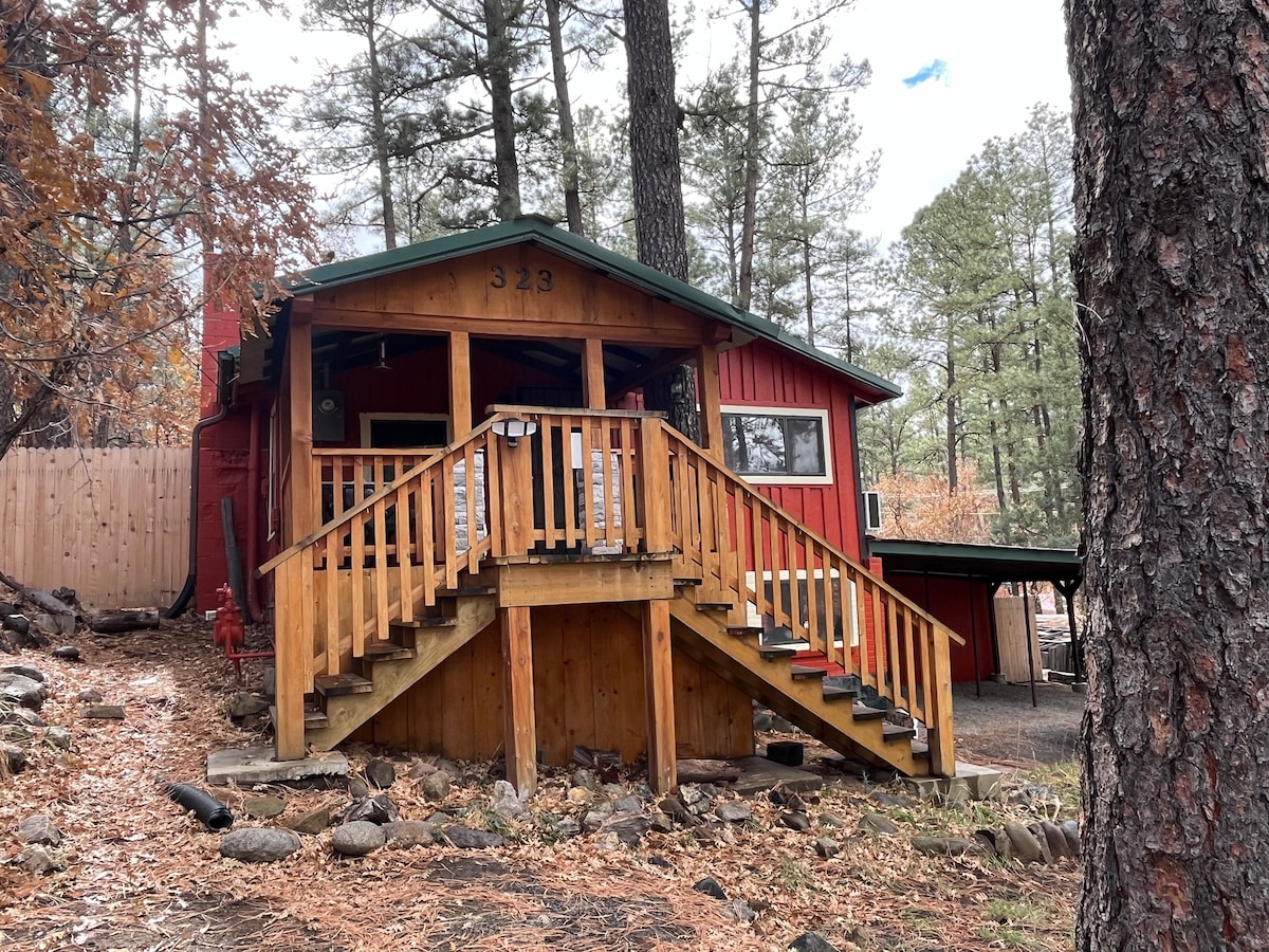 A rustic cabin exterior is highlighted, featuring a welcoming wooden porch with sturdy handrails. The vibrant red walls contrast with the natural surroundings, and tall pine trees provide a serene backdrop. Steps lead up to the entrance, inviting guests to explore the cozy interior.