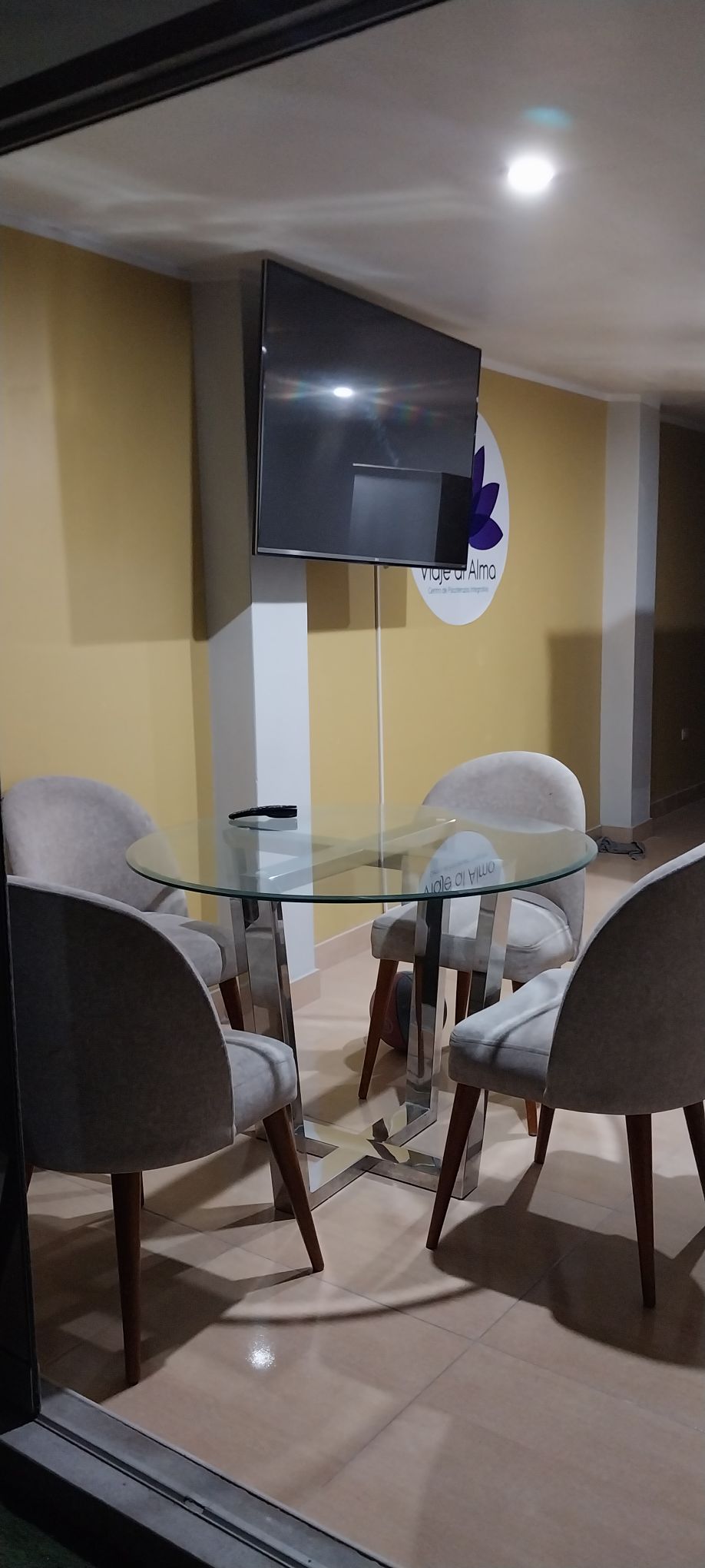 A modern dining area is featured, consisting of a glass-top table surrounded by four upholstered chairs. A flat-screen television is mounted on the wall, with a calming yellow backdrop enhancing the space.