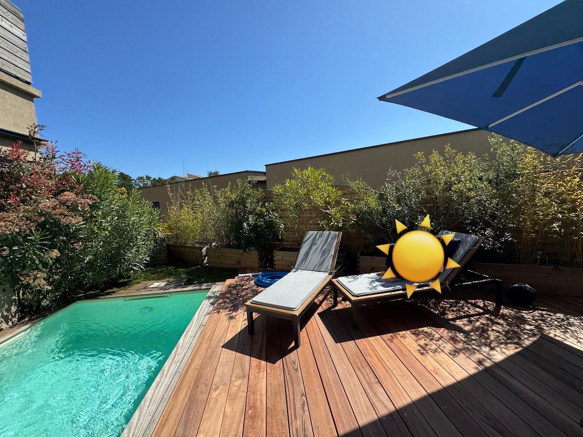 A wooden terrace features two sun loungers positioned beside a private pool. Surrounding greenery adds to the natural ambiance, while bright sunlight enhances the inviting atmosphere. The clear water of the pool reflects the bright blue sky above.