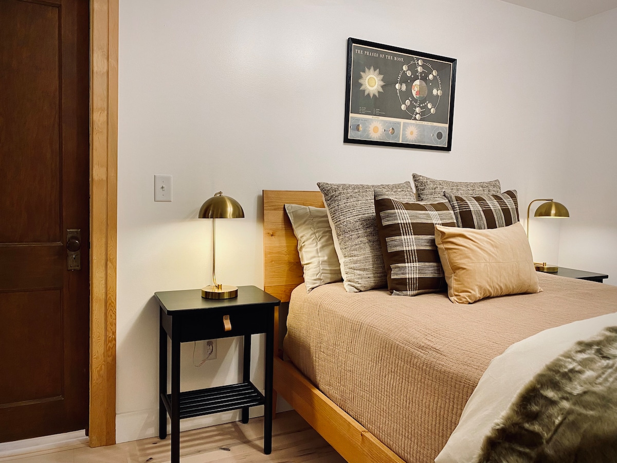 Bedroom 1 with en-suite bathroom. A sophisticated blend of rich earthy colors, woven plaid throw pillows and a Scandinavian inspired bed frame handmade by Amish furniture artisans in Pennsylvania.
