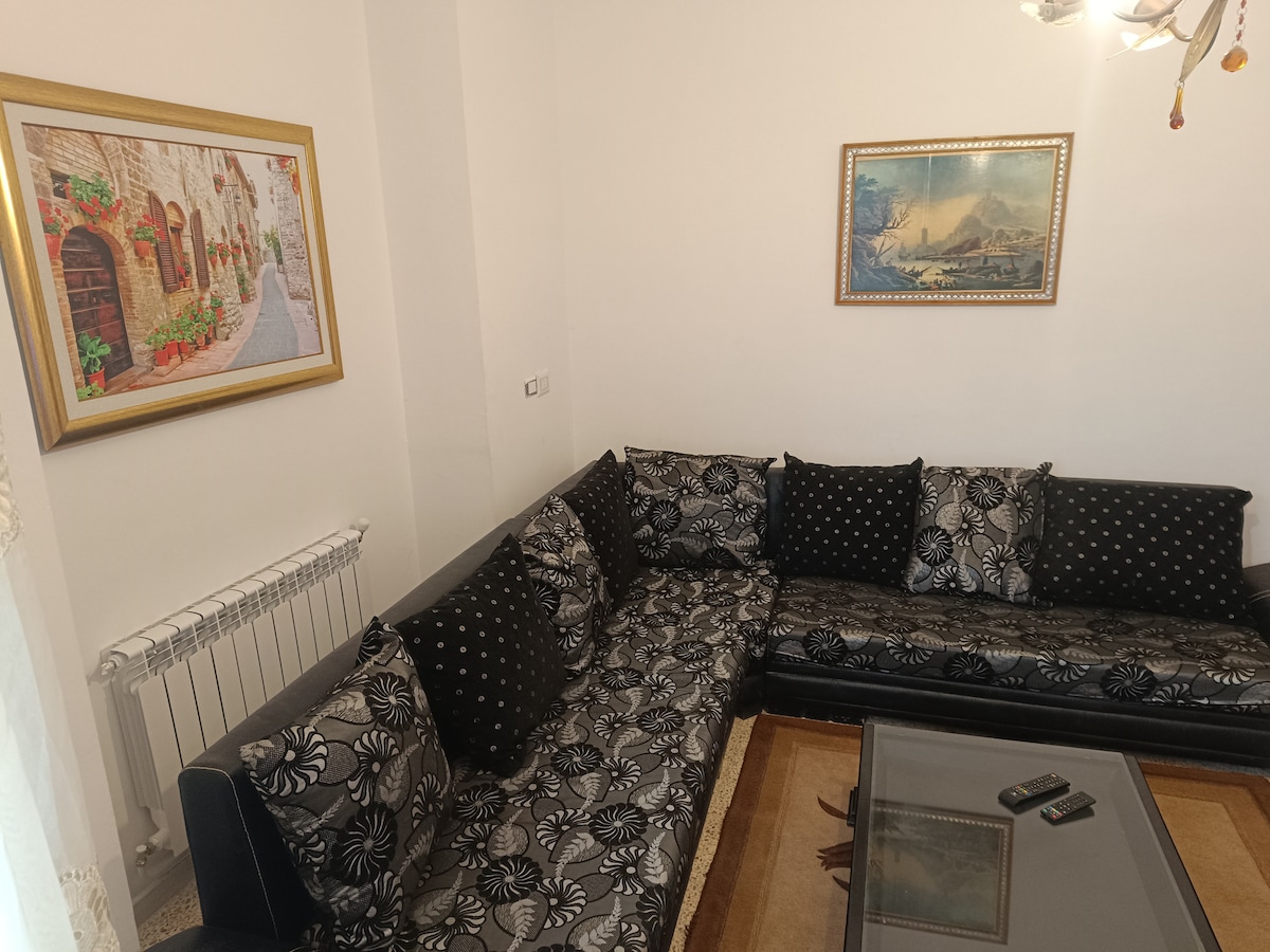 A comfortable seating area is featured, furnished with a large, patterned sofa adorned with decorative cushions. A glass coffee table rests at the center, while two framed artworks hang on the walls, adding visual interest to the space.