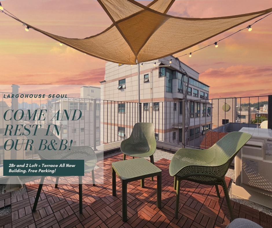 An outdoor terrace features modern green chairs arranged on a brick floor, complemented by a sail shade overhead. Strings of lights add a soft glow, while a glimpse of the city skyline is visible in the background under a pastel sky.