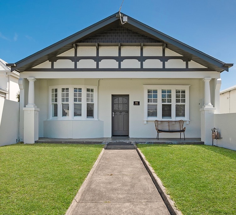 The exterior of a charming three-bedroom house showcases a welcoming façade with distinct architectural features. A neatly paved pathway leads to the front door. Surrounding the entrance, well-maintained grass adds to the inviting atmosphere. Large windows provide ample natural light to the interior.