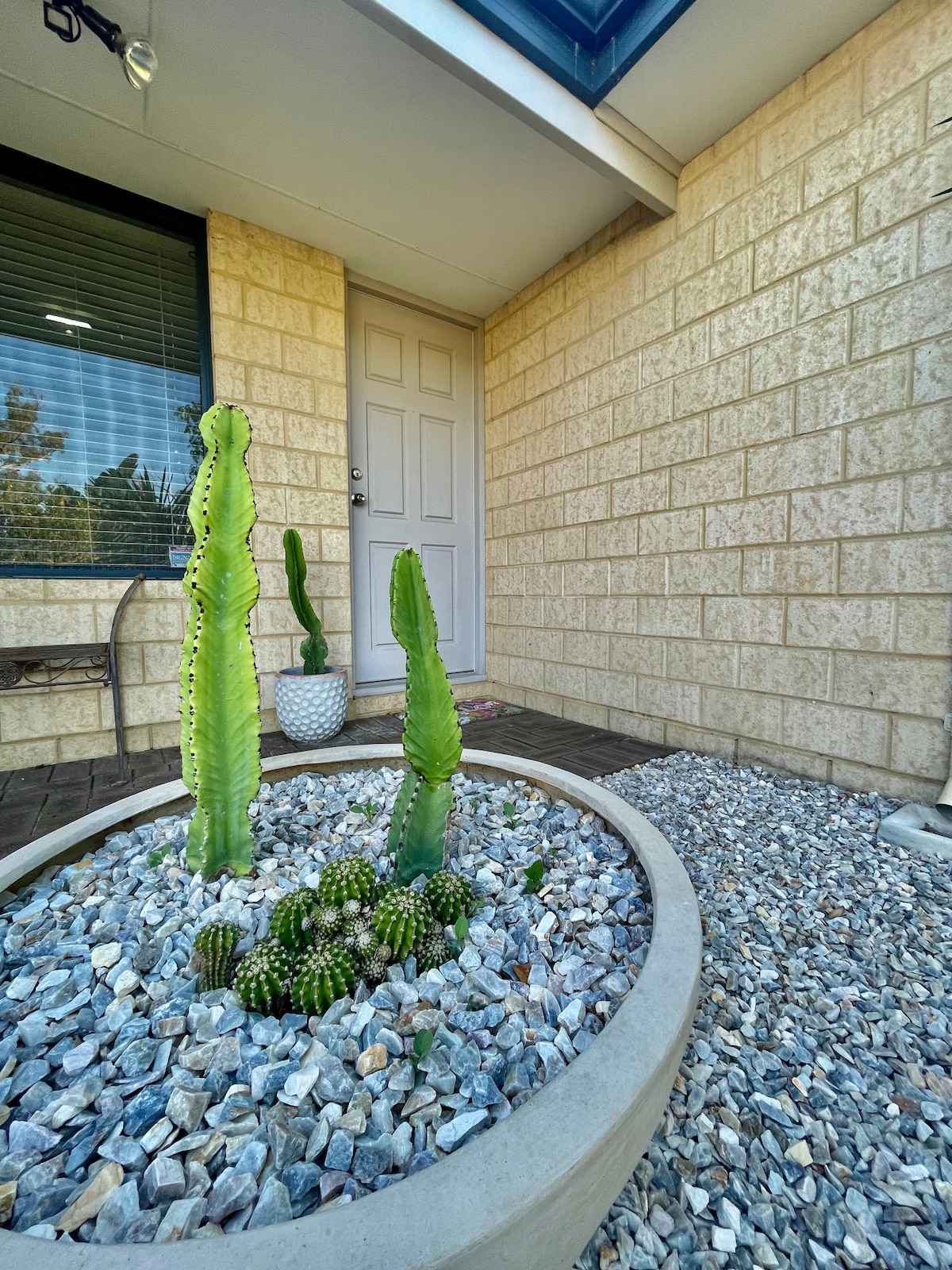 A welcoming entryway features a circular planter filled with various cacti and gravel, providing a modern touch. The textured stone walls and wooden flooring are complemented by a door framed by large windows, inviting natural light into the space.