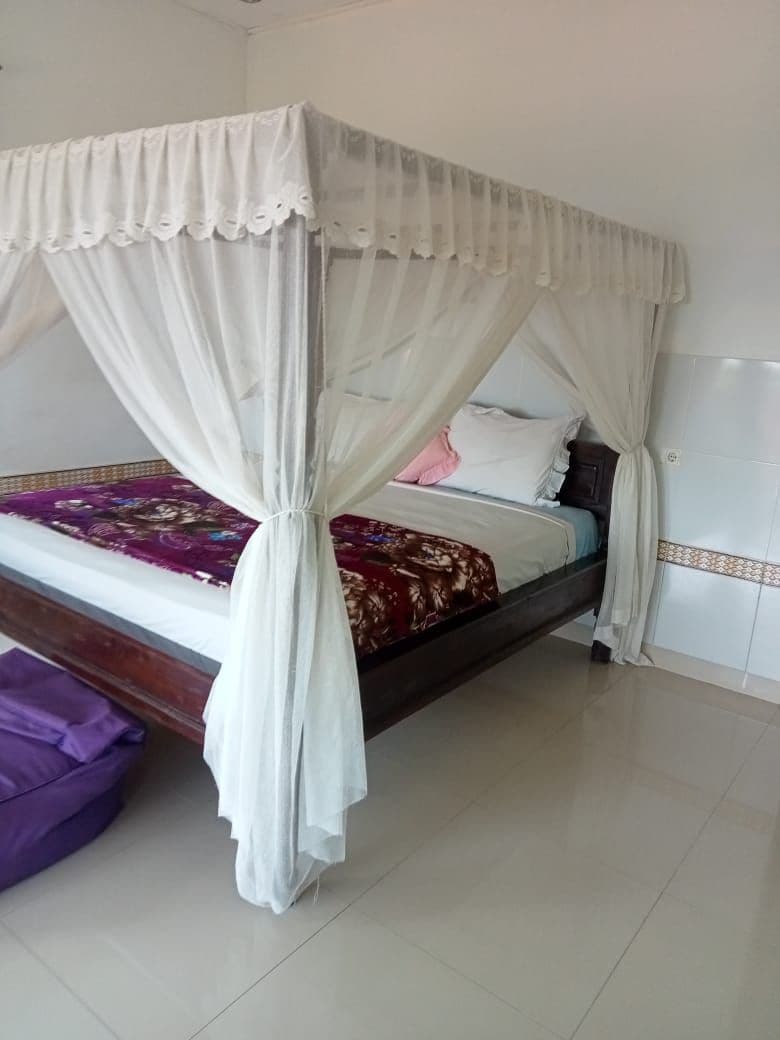 A spacious bed with a decorative canopy is situated in the room, surrounded by sheer white curtains. Soft bedding with a colorful throw is arranged neatly, and a plush beanbag chair is placed nearby on glossy floor tiles.