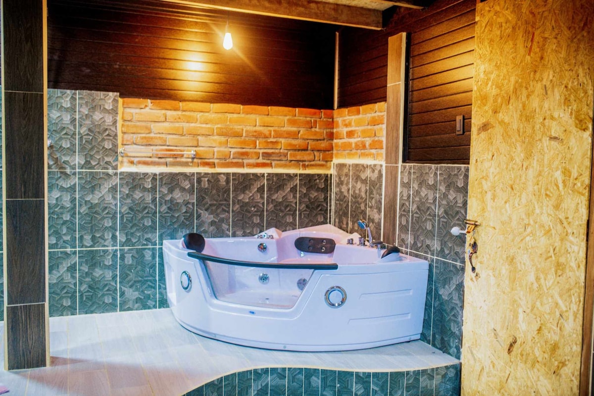 A well-appointed jacuzzi is set against a backdrop of textured brick and dark wooden panels. The spacious tub features various controls and jets, with complementary tiled walls creating a relaxing environment.