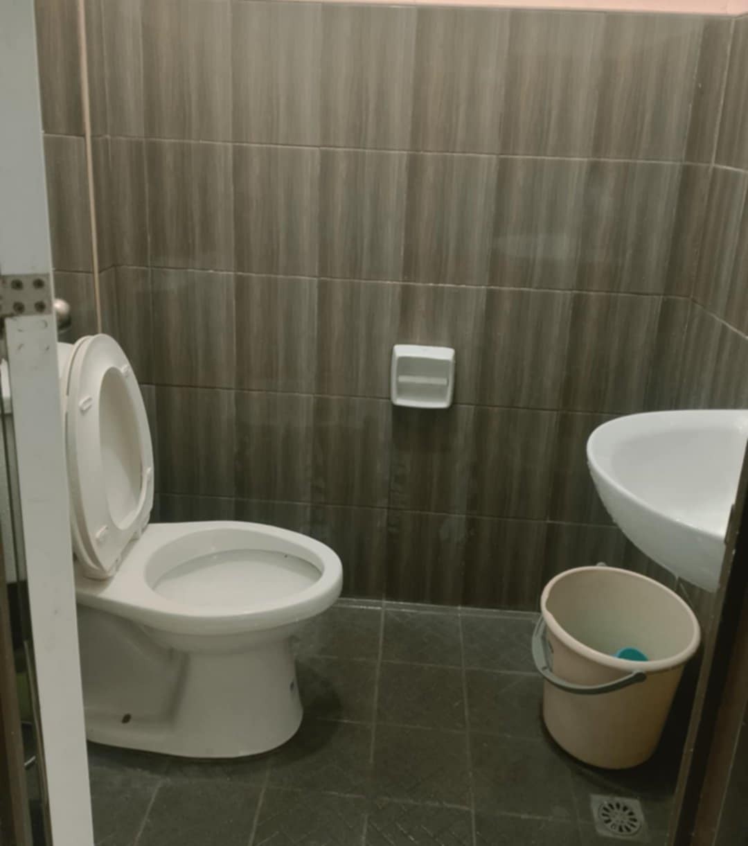A compact bathroom is shown, featuring a white toilet and a modern sink mounted on the wall. The walls are clad in brown tile, providing a clean and neutral aesthetic. A wastebasket is positioned on the floor, offering convenience for guests.