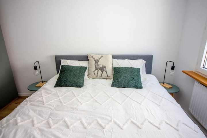 Cosy alpine double bedroom with premium white linen, forest green accents and charming stag cushion detail — private bedroom in Leukerbad vacation rental Swiss Alps