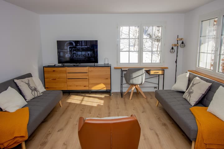 Bright alpine living room with smart TV, dedicated workspace desk and warm wooden furniture — perfect for remote workers and digital nomads staying in Leukerbad