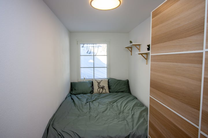 Second private double bedroom with built-in wooden wardrobe and cosy alpine green bedding — sleeps up to 6 guests total in this Leukerbad vacation rental Swiss Alps Valais