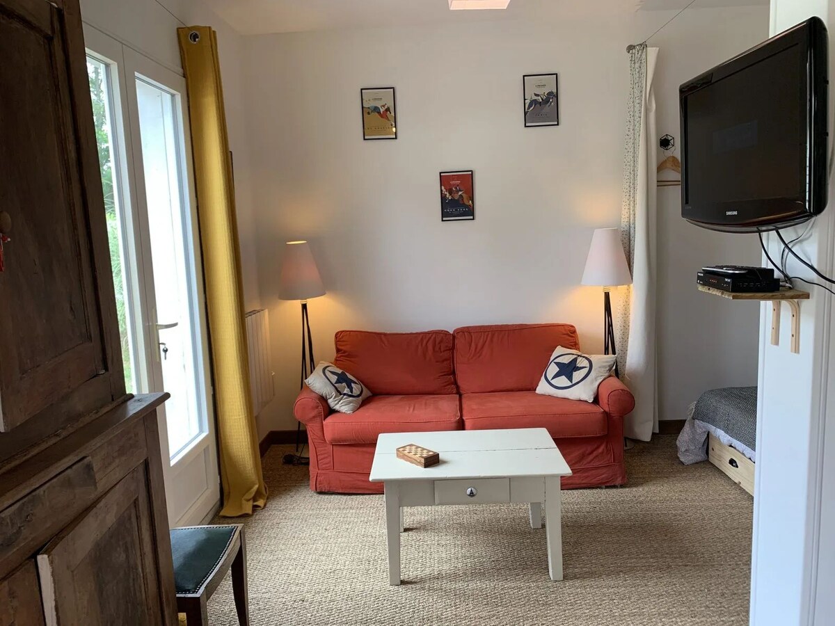 A living area is shown, featuring a bright orange sofa and a light-colored coffee table. Two floor lamps provide ambient lighting. Framed art is displayed on the wall above the sofa, and a television is mounted to the right, complementing the neutral décor.