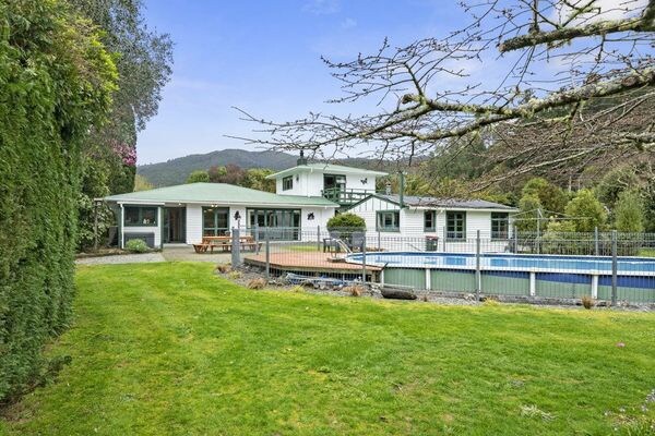 A spacious outdoor area features a well-maintained lawn surrounded by trees. A swimming pool is visible, with a secure fence and deck area for relaxation. The two-story property can be seen in the background, with access to a patio for outdoor dining.
