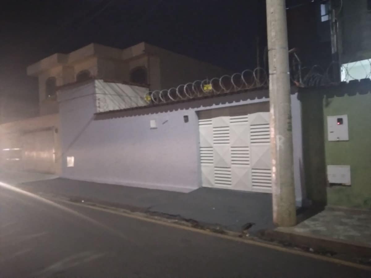 A single-story building is presented with a purple exterior and a securely gated entrance. Barbed wire is visible atop the wall, indicating added security. The area is illuminated by street lighting, providing a subtle glow to the surroundings at night.