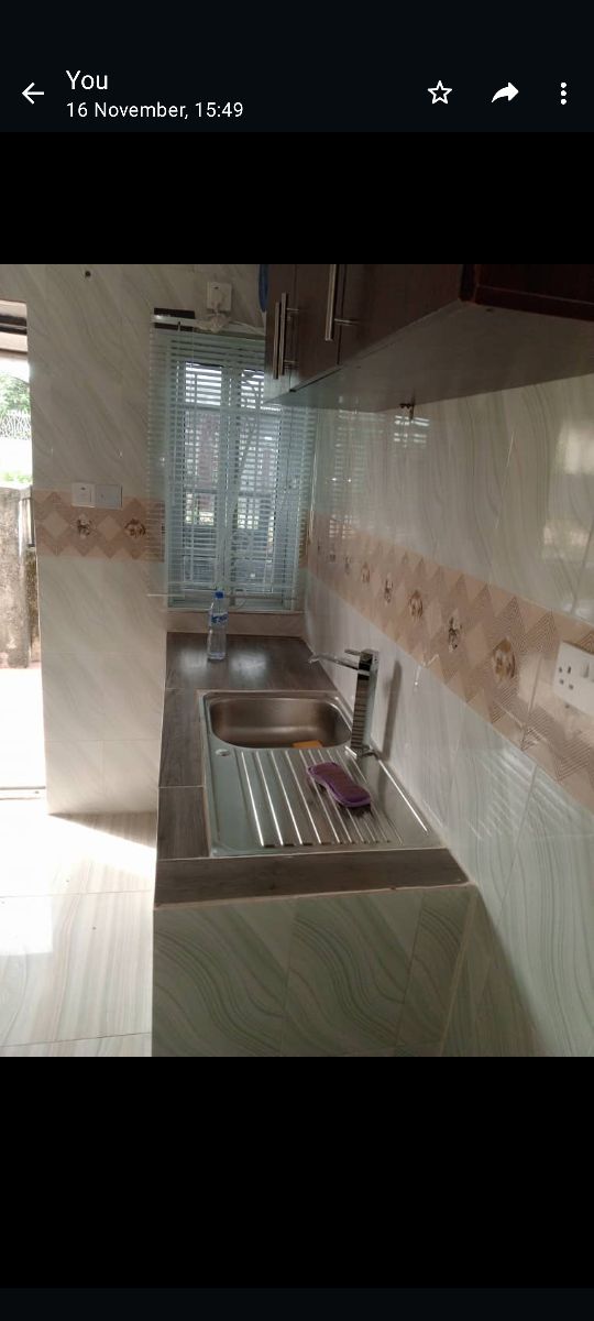 The kitchen area features a modern design with a stainless steel sink and a countertop that allows for food preparation. Natural light filters through the window, enhancing the space. Wall cabinetry provides storage, while tiled walls create a clean, functional environment.