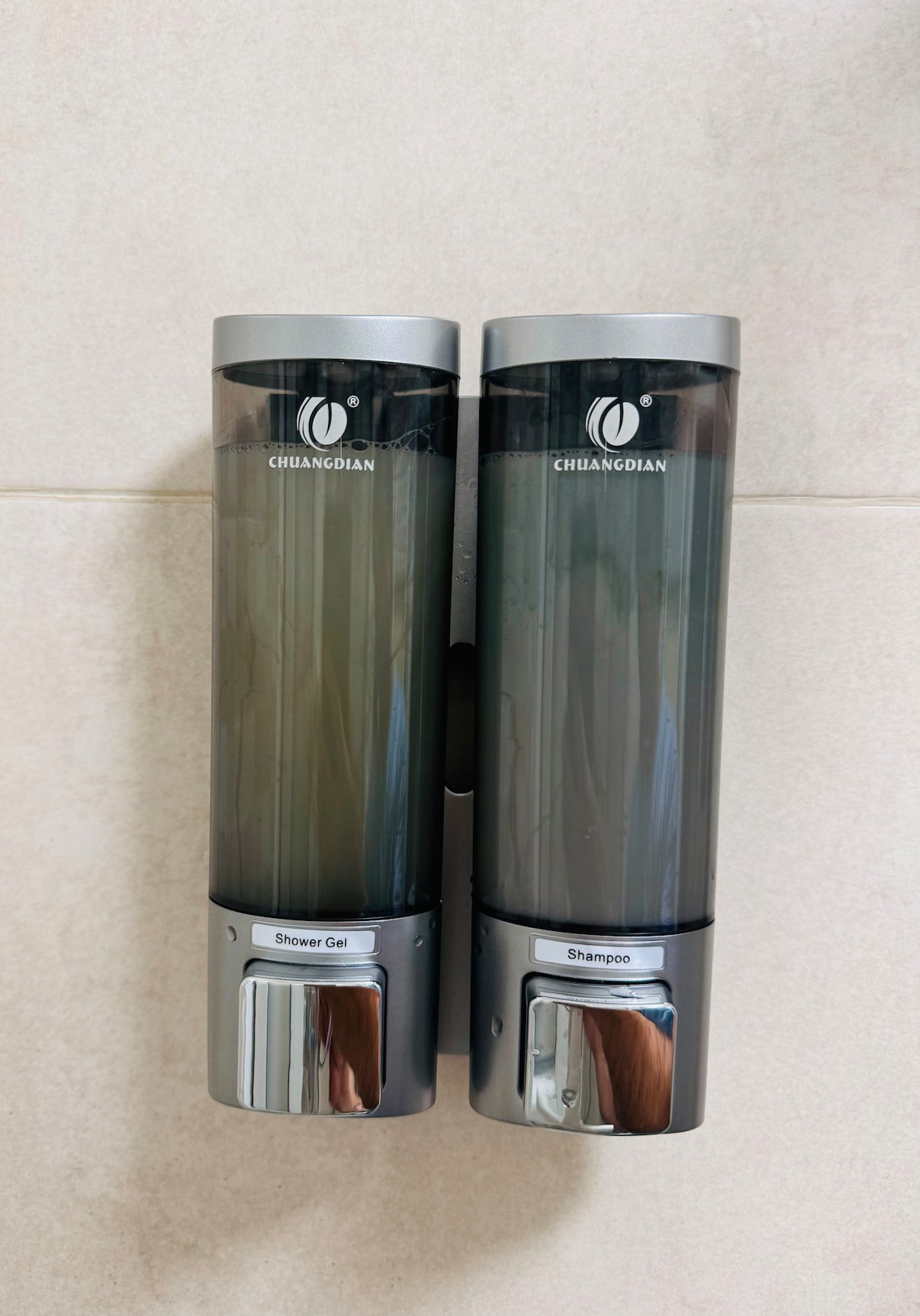 Two wall-mounted dispensers are visible, containing shower gel and shampoo. Each dispenser has a sleek design with a transparent reservoir, allowing for easy identification of the contents. The dispensers are installed at an accessible height, providing convenience for users.