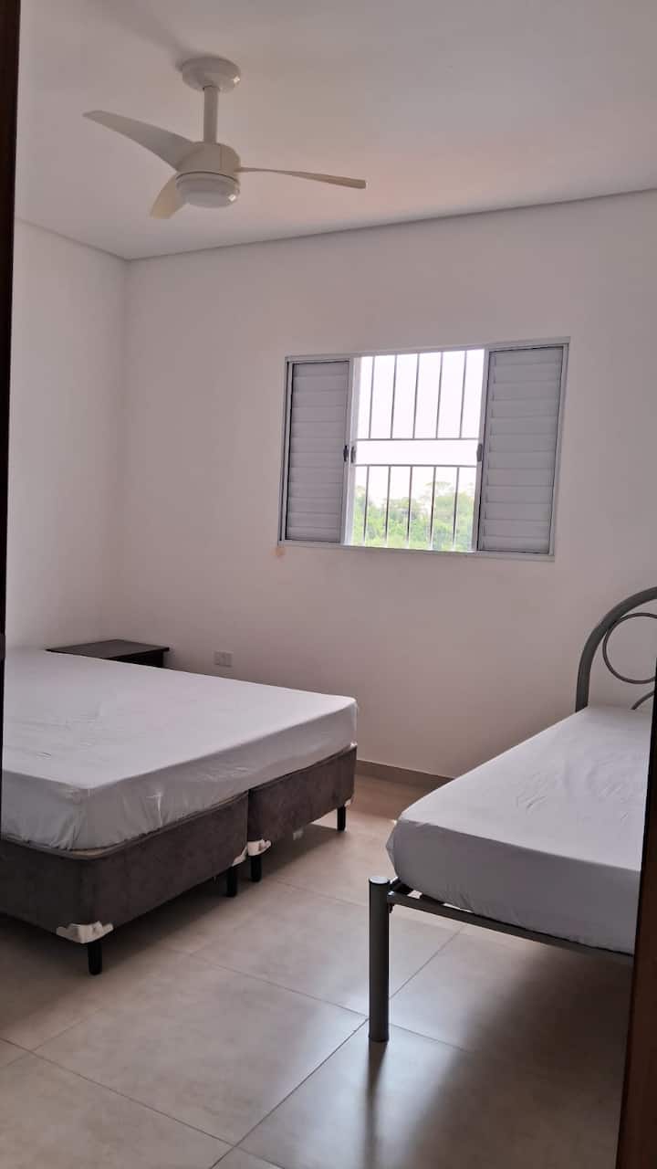 Tretia spálňa na druhom poschodí s manželskou posteľou, samostatnou posteľou, stropným ventilátorom a stojanom na batožinu.