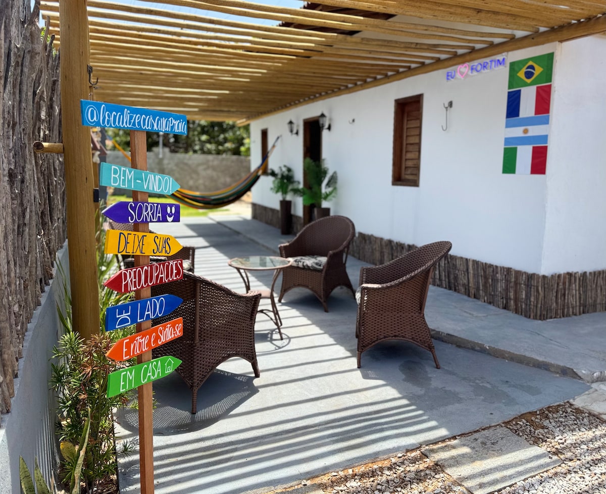 A welcoming outdoor space is highlighted by a hammock and two wicker chairs surrounding a small table. Colorful signs providing cheerful messages adorn the area, while flags from Brazil and Argentina are displayed on the wall, adding a touch of cultural interest.