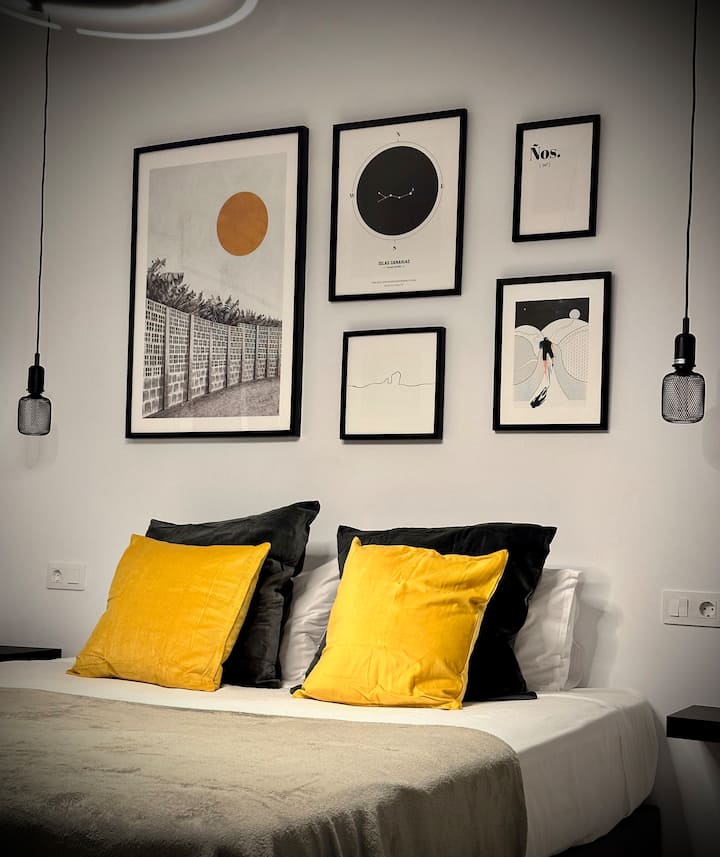 Descansa en un dormitorio de estilo industrial con alma canaria, donde los tonos grises recuerdan la piedra de la costa y las lámparas negras crean un ambiente íntimo. Un refugio perfecto para relajarte y sentir la esencia auténtica del norte.

