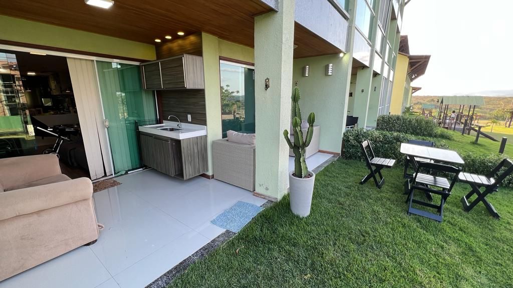 An outdoor area features a small dining table and chairs on lush green grass. A modern kitchenette is visible with cabinets and a sink. A comfortable seating area is situated next to a large window, providing a connection between indoor and outdoor spaces.