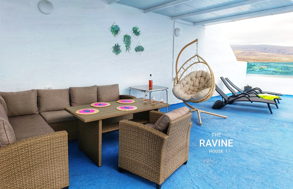 A spacious terrace is presented, featuring a comfortable seating area with wicker furniture and a table set with colorful placemats. A hanging chair offers a unique seating option, while lounge chairs are positioned for sunbathing. Scenic vistas extend beyond the terrace.