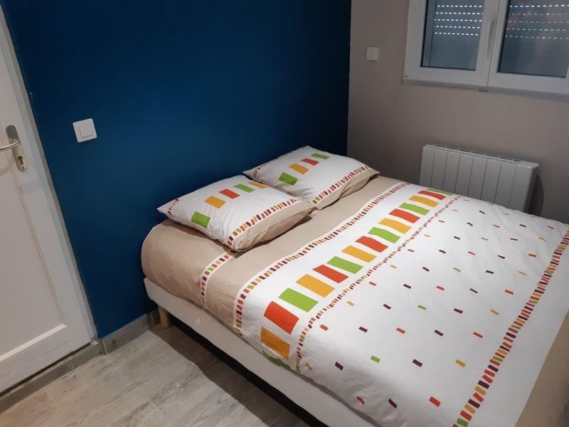 A cozy sleeping area features a bed with a colorful duvet and matching pillows against a contrasting blue wall. Light-colored flooring complements the space, while natural light enters through a nearby window, adding a bright touch to the room.
